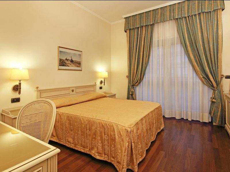 Chambre d'hôtel élégante avec grand lit double, bureau et fenêtre avec rideaux.