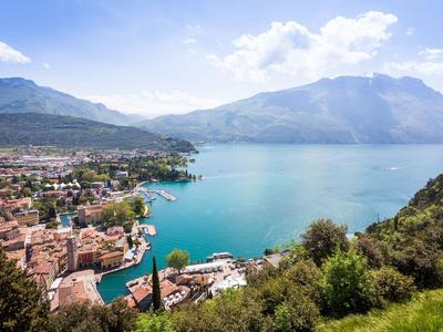 Vista di una città sul lago con montagne sullo sfondo sotto un cielo azzurro.