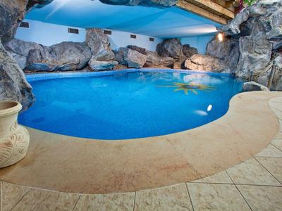 Piccola piscina interna con acqua blu, circondata da rocce e soffitto in legno.
