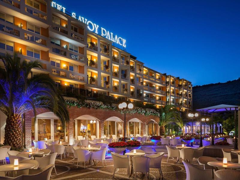 Luxury hotel with outdoor seating, lit tables, and palm trees at dusk.