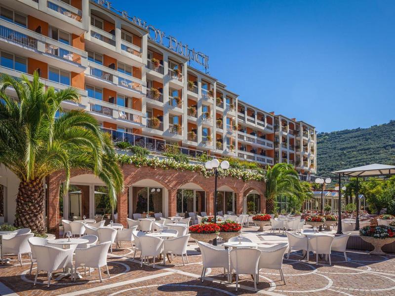 Hotel terrace with white chairs, tables, and palm trees under a clear blue sky.
