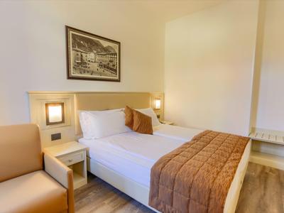 Gemütliches Hotelzimmer mit Doppelbett, braunen Bettdecken, einem beigen Sessel und Wandbild.