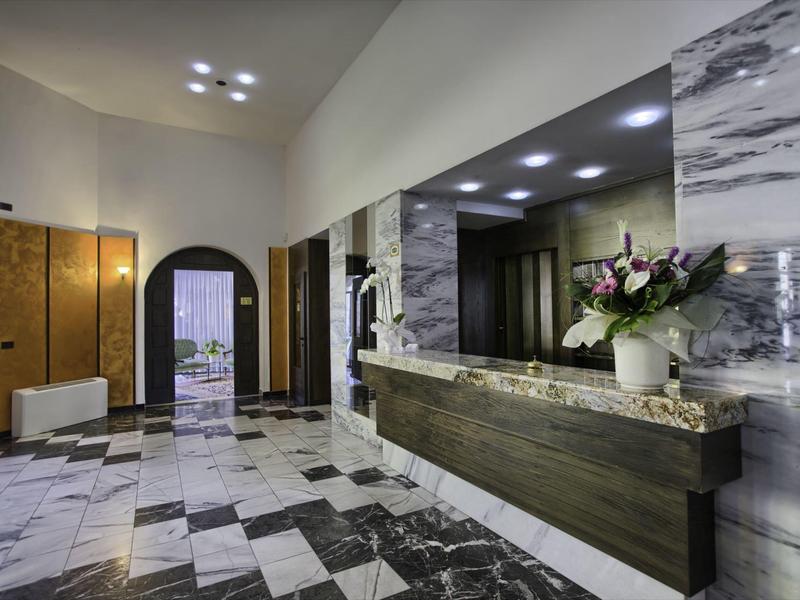 Moderne hotel lobby met marmeren vloer, donkere receptiebalie en bloemendecoratie.