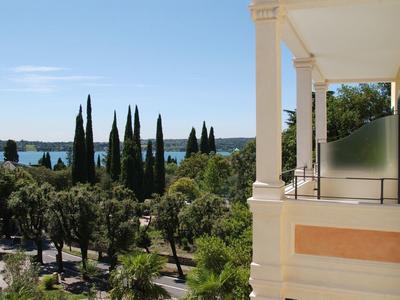 Uitzicht vanaf een hotelterras over groene bomen en de blauwe zee onder een heldere lucht.