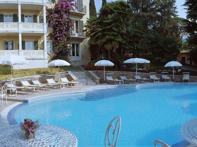 Espace piscine avec parasols bleus et chaises blanches devant un hôtel à plusieurs étages.