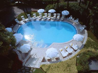 Rond hotelzwembad omringd door witte ligstoelen en parasols in een tuin.