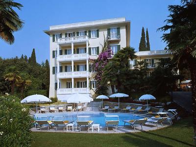 Bâtiment d'hôtel moderne avec piscine, chaises longues et parasols blancs dans un jardin.