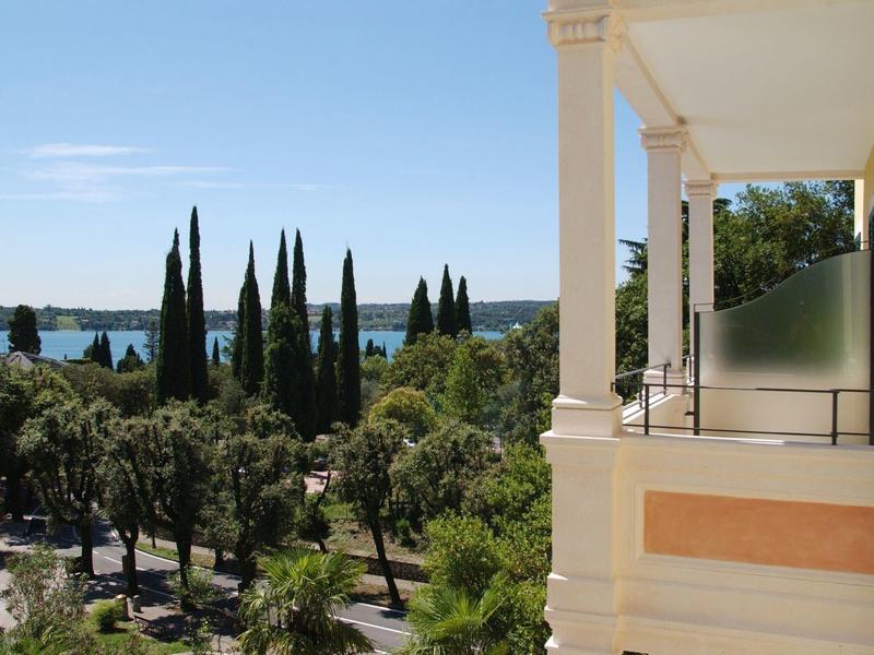 Uitzicht vanaf een hotelterras over groene bomen en de blauwe zee onder een heldere lucht.