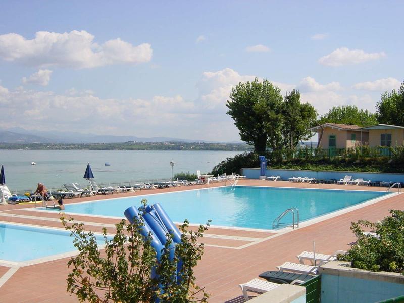 Großer Außenpool mit blauer Wasserfläche, Liegestühlen und schattenspendenden Sonnenschirmen am Seeufer.