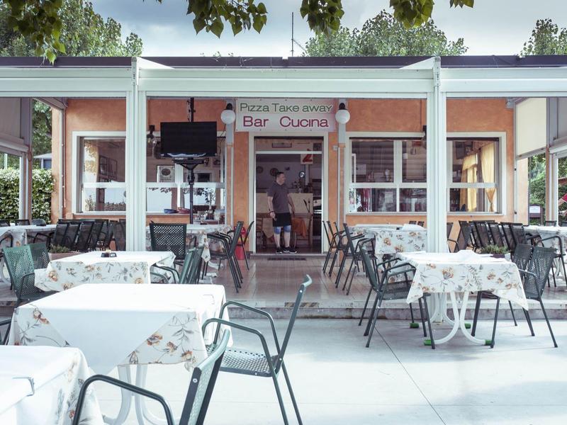 Außenbereich eines Restaurants mit weißen Tischtüchern und schwarzen Stühlen unter Bäumen.