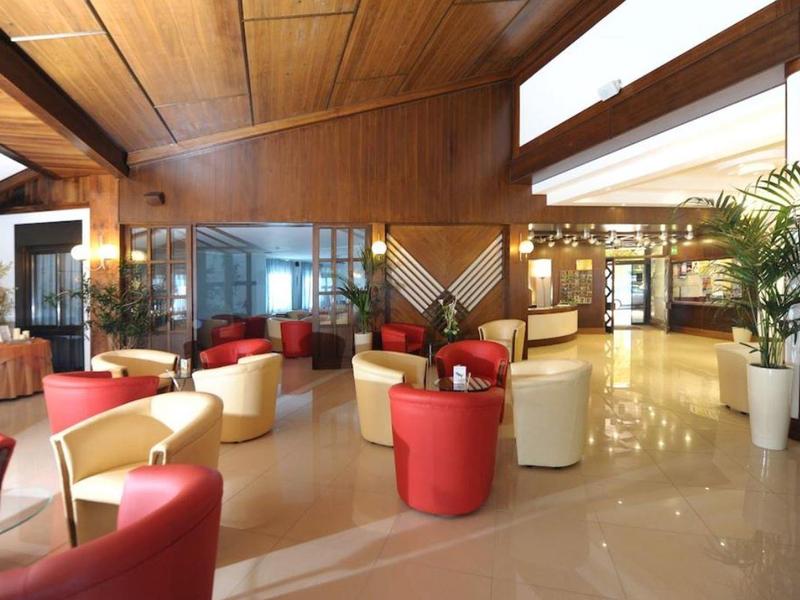 Salon d'hôtel avec fauteuils rouges et beiges, murs en bois et grandes fenêtres.