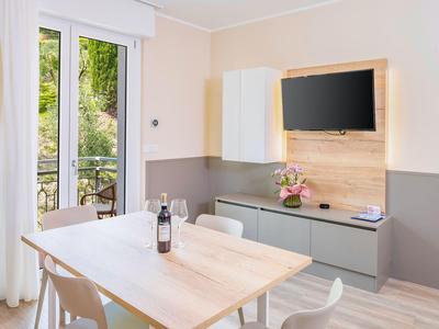 Sala da pranzo moderna con tavolo in legno, sedie, TV a schermo piatto e vista su balcone con giardino