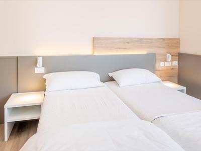 Chambre d'hôtel lumineuse avec deux lits simples, literie blanche et tables de chevet.