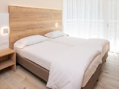 Hell eingerichtetes Schlafzimmer mit großem Doppelbett, Holz-Kopfteil, Nachttisch und hellen Vorhängen.