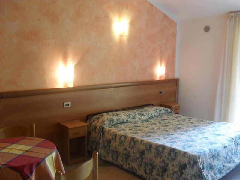 Una camera d'hotel con un letto matrimoniale, comodino e un piccolo tavolo con una tovaglia colorata.