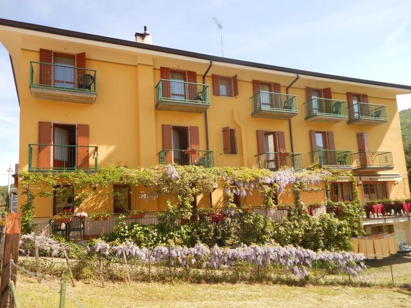 Edificio dell'hotel giallo di tre piani con balconi e vigneti fioriti davanti.