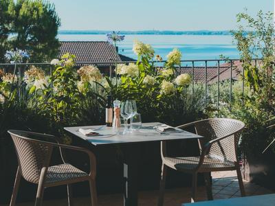 Terasa se stolem a čtyřmi židlemi před kvetoucími rostlinami a výhledem na jezero.
