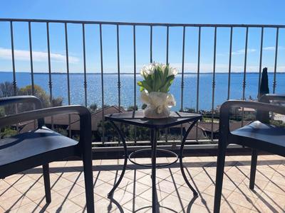 Balkon se stolem, květinami a dvěma židlemi s výhledem na moře pod modrou oblohou