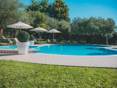 Rechteckiger Swimmingpool mit Sonnenschirmen und umgeben von Bäumen und Rasenfläche.