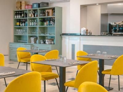 Moderní kavárna se žlutými židlemi, šedými stoly a regály s nápoji v pozadí.