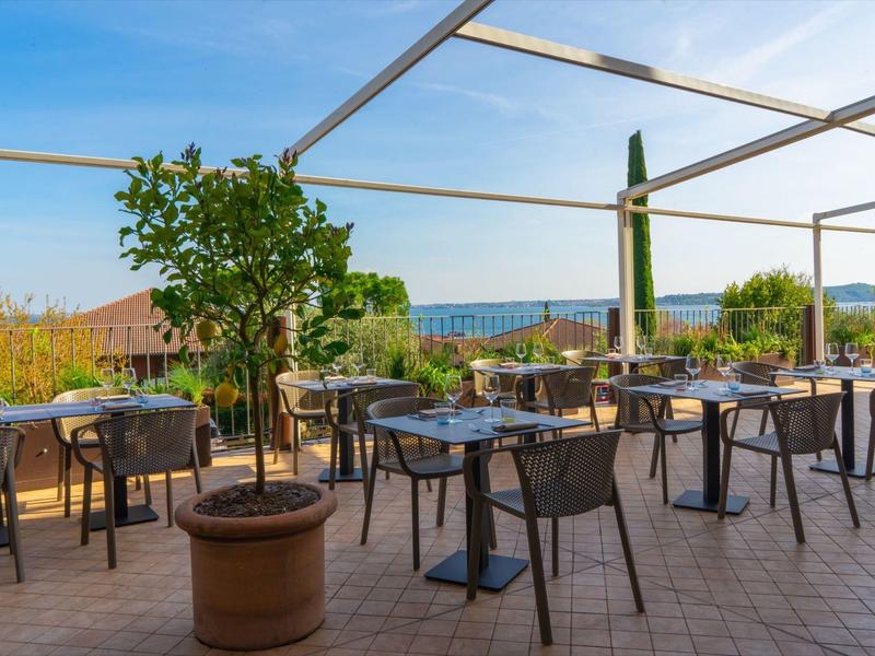 Terasa s stoly, židlemi a slunečníky s výhledem na vinice a kopce.