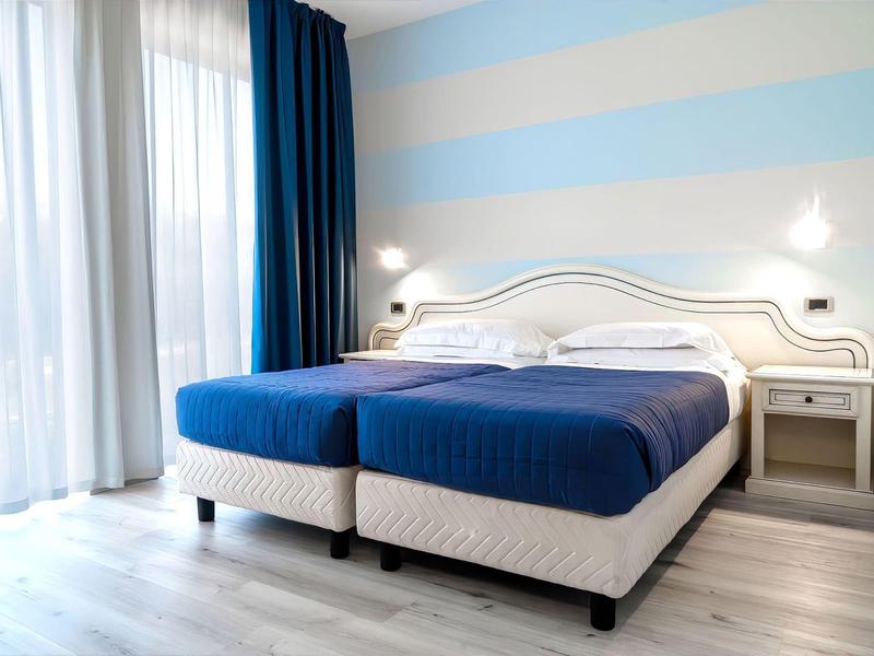 Moderní hotelový pokoj se dvěma jednolůžky, modrým povlečením a světlými závěsy.