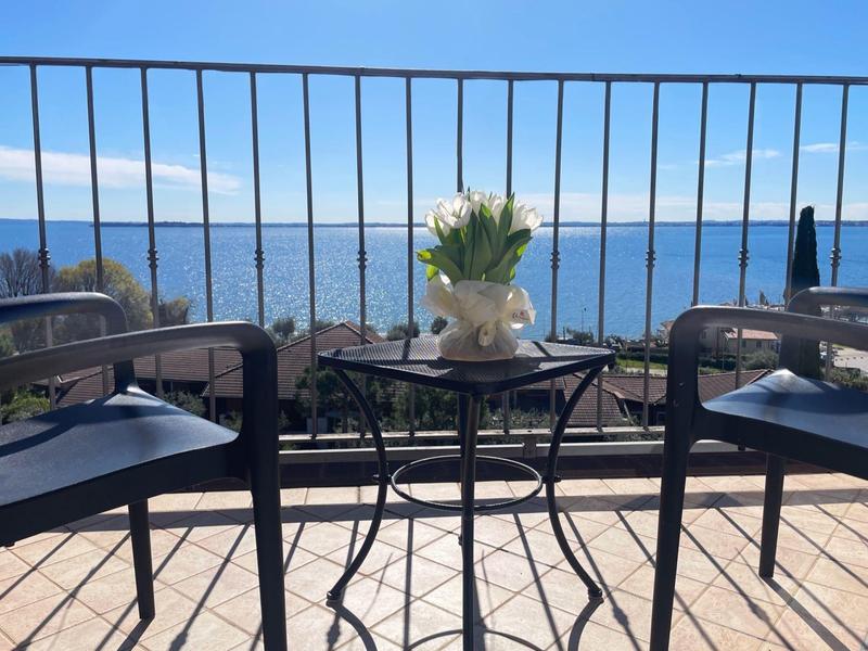 Balkon se stolem, květinami a dvěma židlemi s výhledem na moře pod modrou oblohou