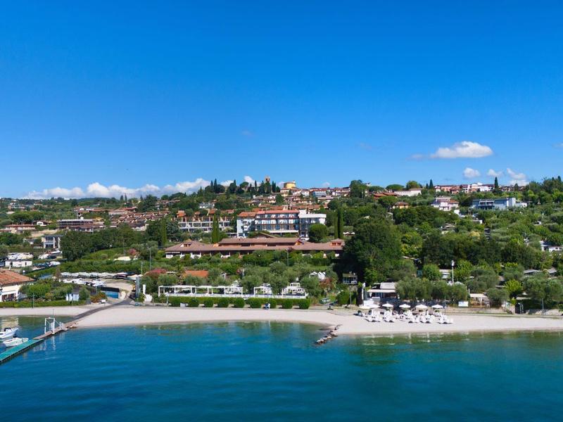 Pobřežní krajina s pláží, hotelovým areálem a jasně modrou vodou pod čistou oblohou.