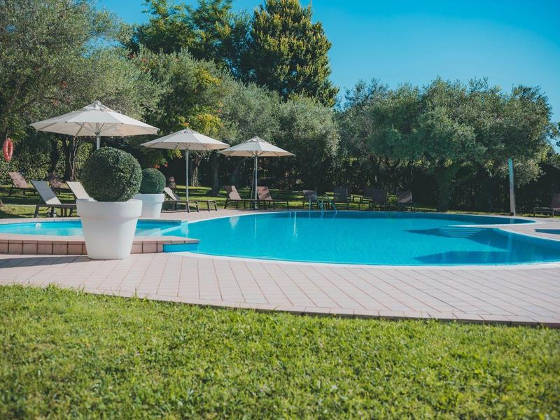 Vstřícný hotelový bazén s slunečníky a zeleným okolím pod jasnou oblohou.