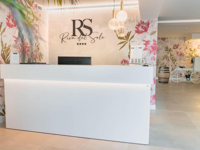 Moderní hotelová recepce s bílým pultem a květinovou výzdobou na zdi.