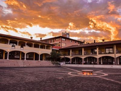 Großer Innenhof mit Feuerstelle, umgeben von zweistöckigen Gebäuden bei orangefarbenem Sonnenuntergang.