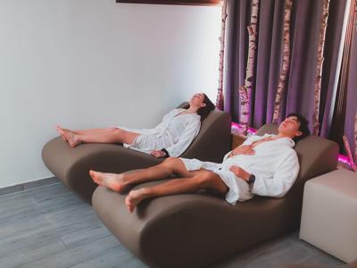 Dwie osoby relaksują się w szlafrokach na leżakach w nowoczesnym pokoju wellness.