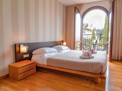 Nowoczesny pokój hotelowy z podwójnym łóżkiem, drewnianą podłogą i widokiem na balkon.