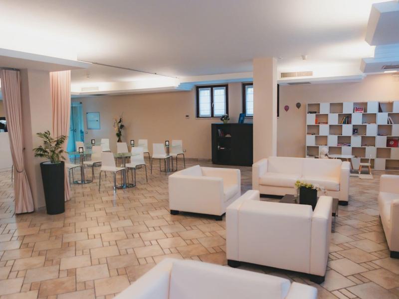 Nowoczesna strefa lounge w hotelu z białymi fotelami i jasną podłogą z płytek