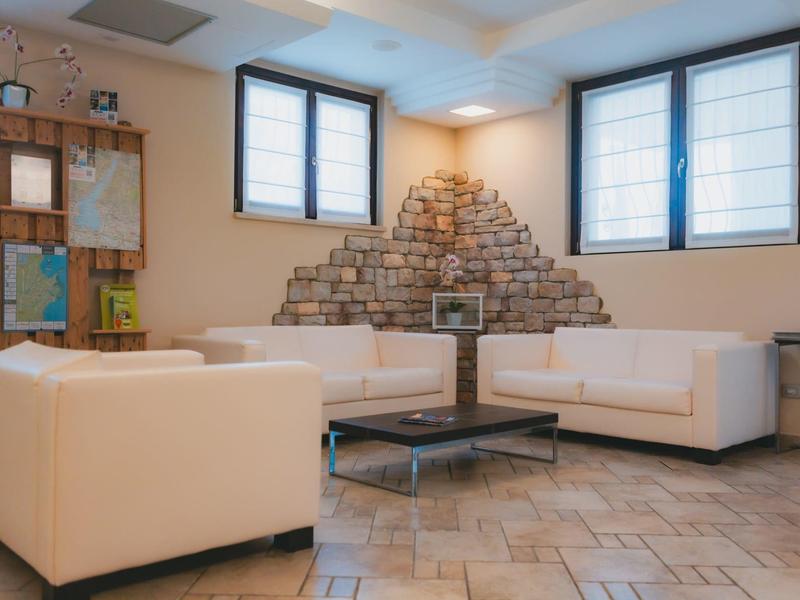 Jasny hol hotelowy z białymi sofami, kominkiem i oknami z roletami.