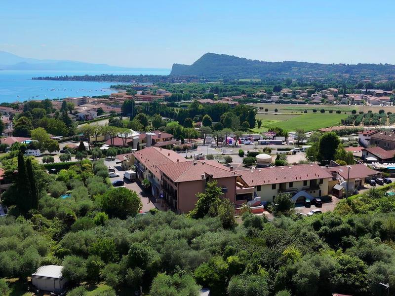 Widok na nadmorską wioskę z czerwonymi dachami, zieloną roślinnością i niebieskim morzem w tle.