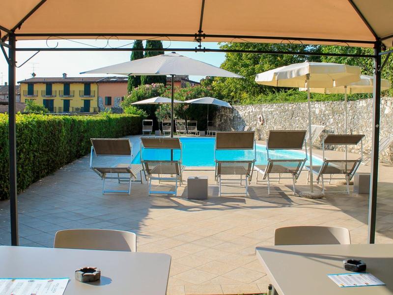 Słoneczny taras z basenem, leżakami i stolikami pod parasolami.