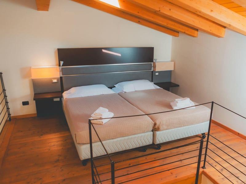 Dwa pojedyncze łóżka z szarą pościelą i drewnianym sufitem w prostym pokoju.