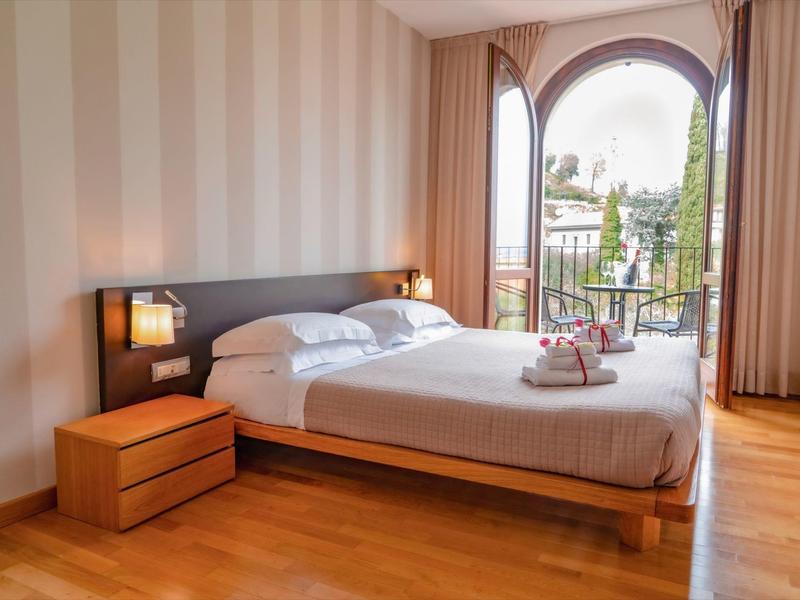 Nowoczesny pokój hotelowy z podwójnym łóżkiem, drewnianą podłogą i widokiem na balkon.