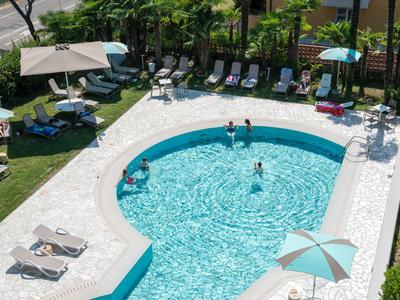 Uitzicht op een zwembad met meerdere mensen, omgeven door ligstoelen en parasols.