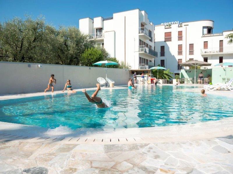 Hotel con piscina all'aperto circondata da edifici bianchi e alberi sotto un cielo sereno.
