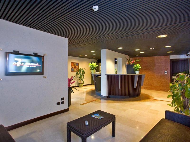 Hall d'hôtel moderne avec réception, canapé, table et plantes décoratives.