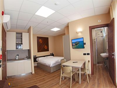 Compacte hotelkamer met tweepersoonsbed, kleine eettafel, kitchenette en aangrenzende badkamer.