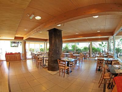 Ristorante luminoso con soffitti in legno, pavimento piastrellato e molti tavoli e sedie.