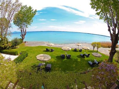 View of a large lawn with seating areas and trees by a lake shore under a blue sky.
