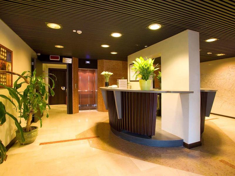 Modern hotel reception with front desk, plants, and warm lighting.