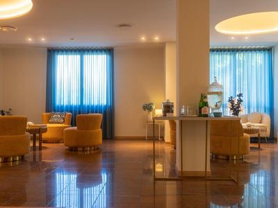 Accogliente area lounge dell'hotel con poltrone arancioni, tavoli e luce delle tende blu.