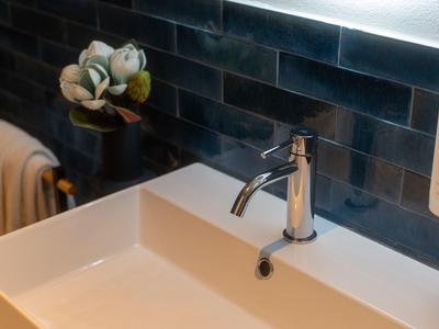 Lavandino bianco moderno con rubinetto monocomando e dispenser di sapone davanti a parete piastrellata nera.