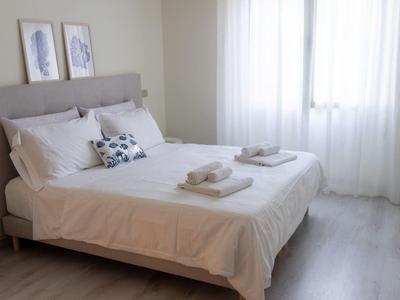 Camera d'albergo luminosa con letto grande, biancheria bianca e finestra con tende.