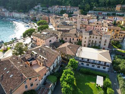 Vista di una città costiera con edifici antichi, una spiaggia e colline boschive sullo sfondo.